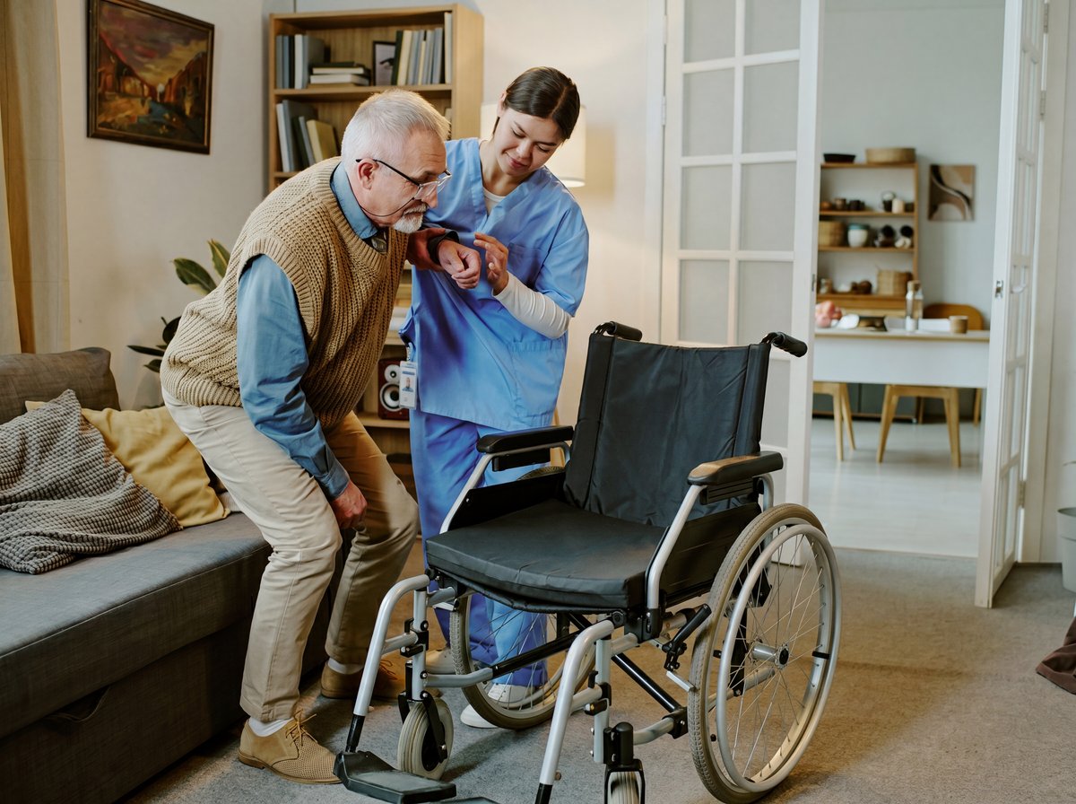 A home-care nurse helping an older man stand and transfer to his wheelchair